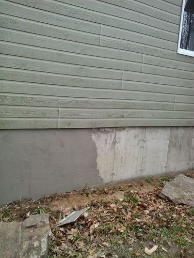 Foundation with old parging peeling away under the wood siding.